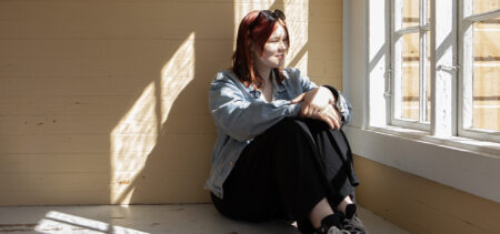 Nuori nainen istuu penkillä ja katsoo ulos ikkunasta auringonpaisteeseen.