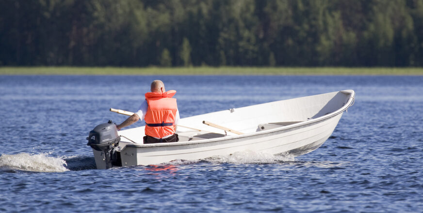 Järvellä pieni vene, jossa perämoottori ja yksi veneilijä pelastusliivit yllään.