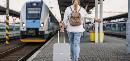 Nainen kävelee juna-asemalla laiturilla kohti lähtevää junaa, vetää matkalaukkua perässään.